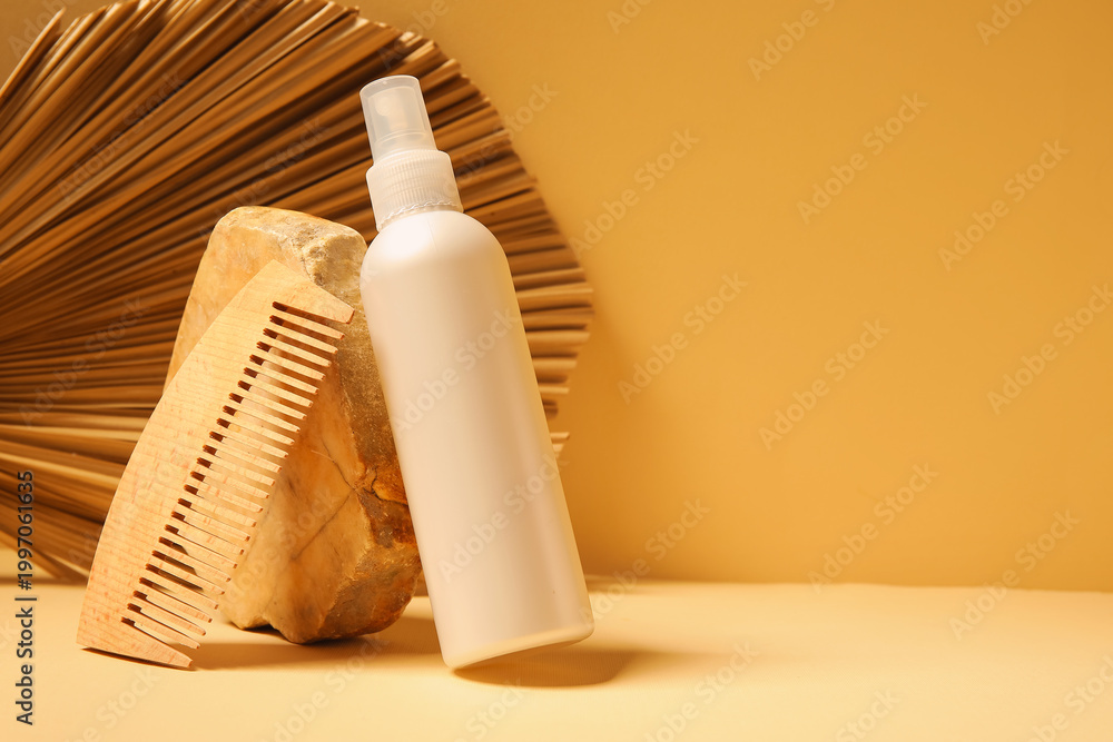 Obraz premium Stone with hair spray, comb and palm leaf on yellow background