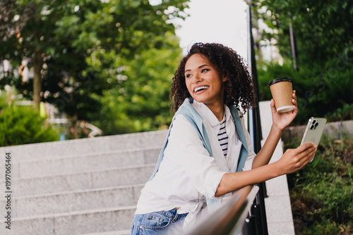 Фотография Smiling young woman on urban steps with coffee cup and phone enjoying a sunny da