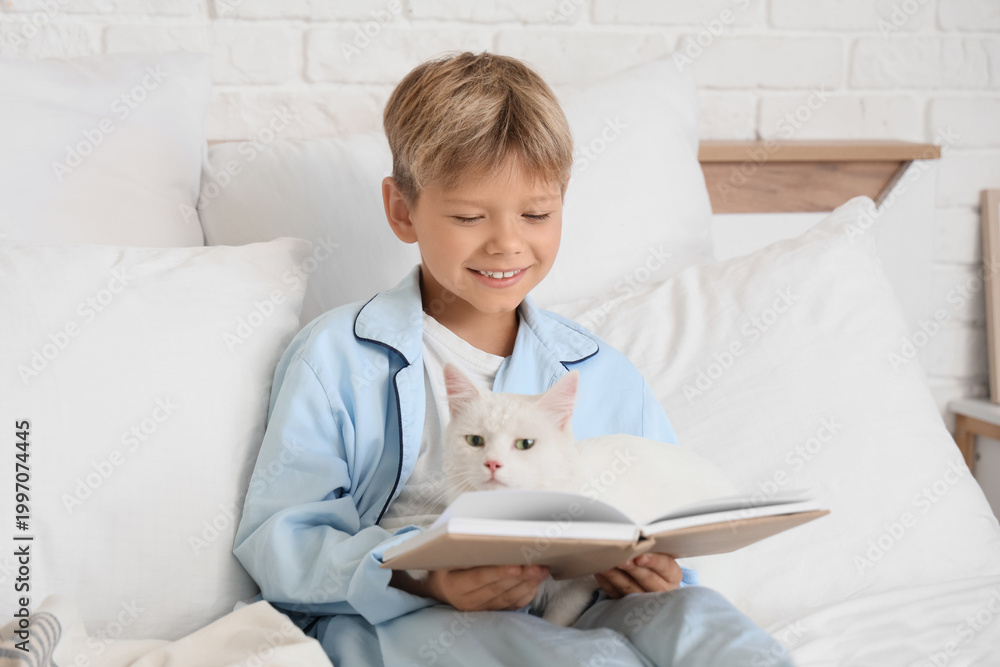 Fototapeta premium Cute little boy with cat reading book in bedroom