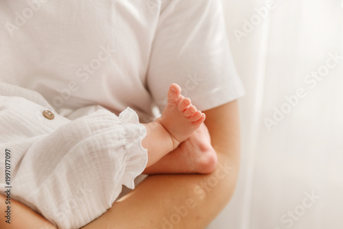 Foto Close-up of tiny newborn baby feet held by mother, tender skin and white cotton clothes