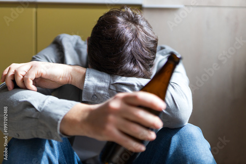Young man holding beer bottle with head down indicating alcohol misuse and emotional distress for awareness poster or campaign banner
