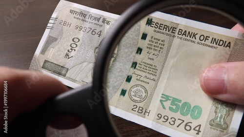 Examination of 500 Indian rupees (INR) cash money with magnfication glass, loupe. Concept of authenticity check, fight against counterfeiting of banknotes, anti fraud measures in India. Close up view.