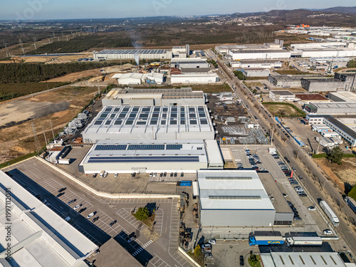Aerial view of sprawling industrial complexes with gleaming solar panels under a vibrant blue sky, contrasting with undeveloped land, Albergaria-a-Velha, Aveiro District, Portugal.