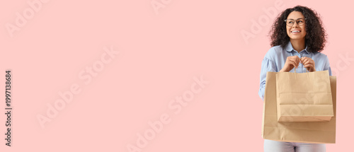 Young African-American woman with paper bags on pink background. Food deliver...