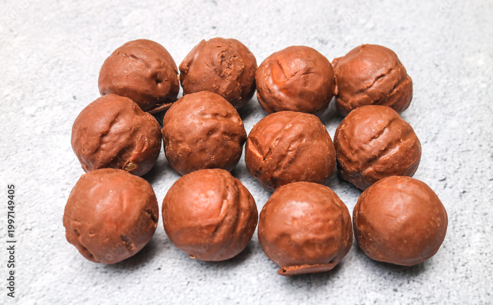 Obraz premium Close up of many chocolate candy balls with broken peanut filling on gray background, top view. Pile of chocolate balls in a bowl.