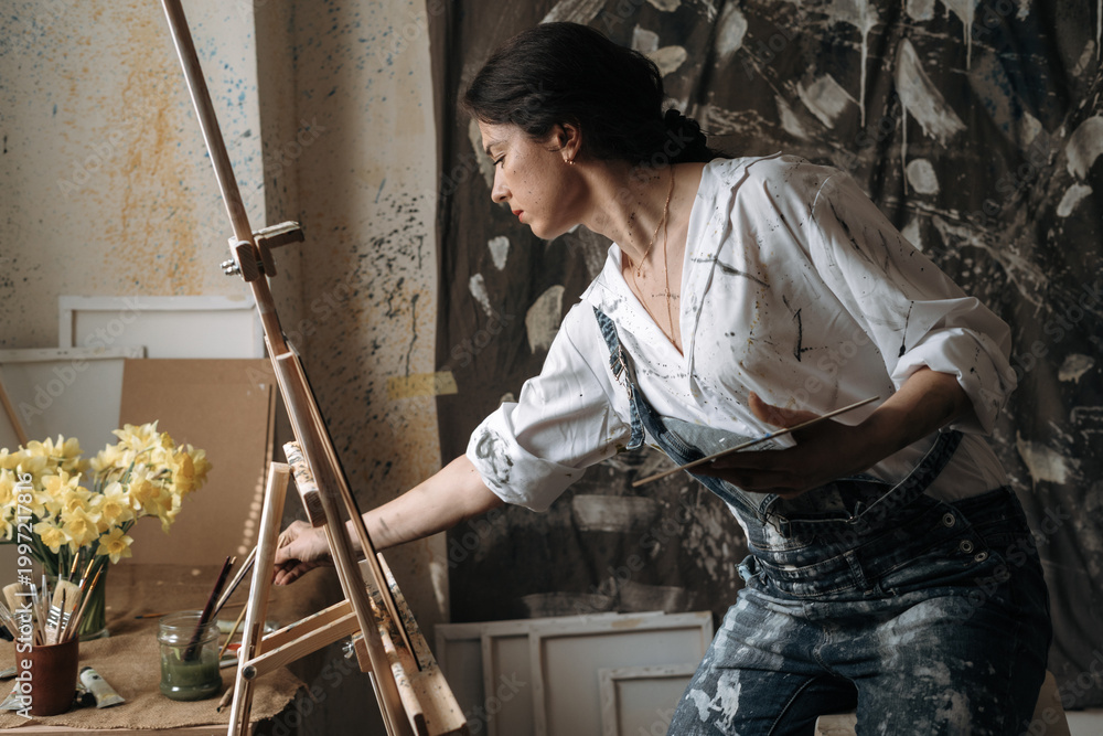 Naklejka premium Brunette woman creating in her art studio. female artist painting on canvas, preparing to creative exhibition. watercolor painter talent.