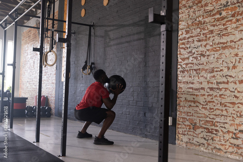 Принти на полотні African American man squatting while holding black medicine ball wearing red shi