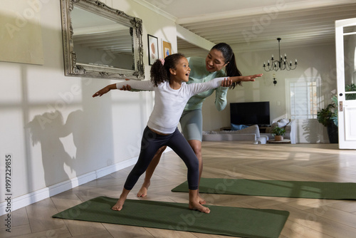 Obraz na plátně Asian woman gently guiding African American girl practicing yoga on green mat in
