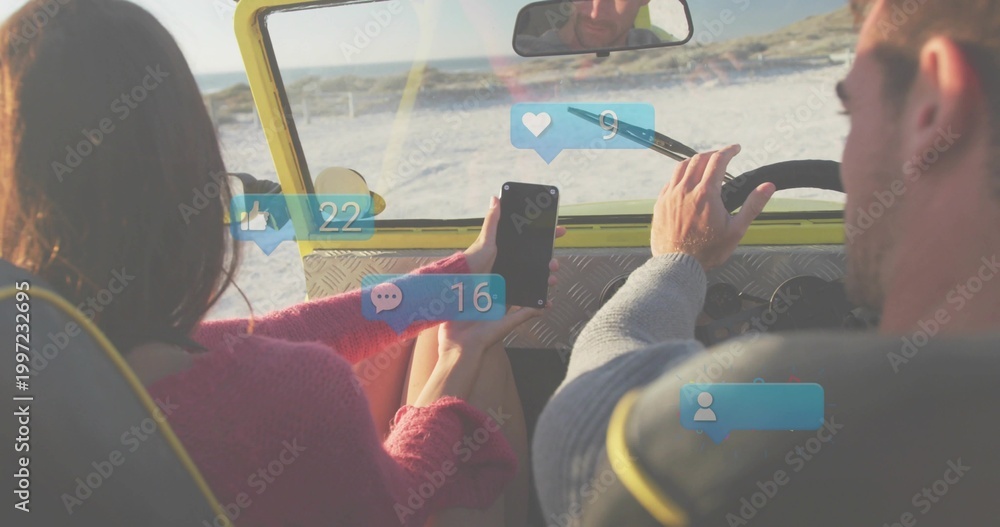 Obraz premium Driving couple in yellow drop-top along beach, passenger in pink sweater holding phone with badges