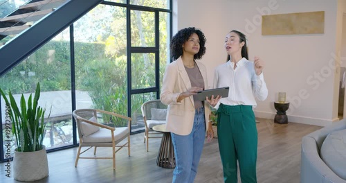 Diverse female colleagues consulting tablet in living room after spotting ceiling feature, pointing