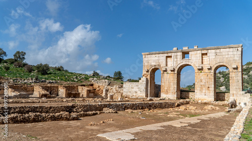 The Roman Arch of Modestus rising over excavated ruins at ancient Patara archaeological site, Lycia, Turkey. A well-preserved triumphal gate under a vivid blue sky