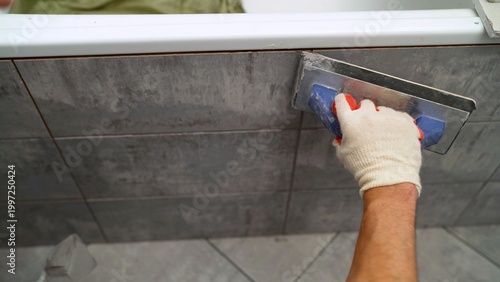 Billede på lærred Close up of worker applying gray grout to new ceramic tiles on wall