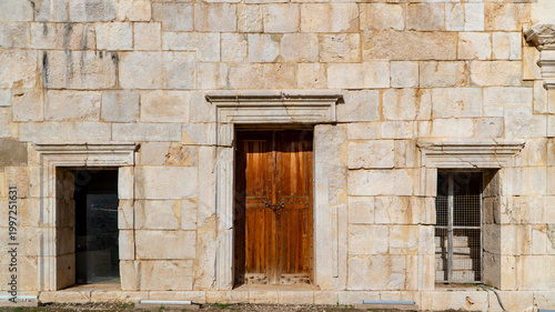 Ancient limestone facade with a locked wooden double door and framed window niches at the Patara archaeological site, Antalya, Turkey