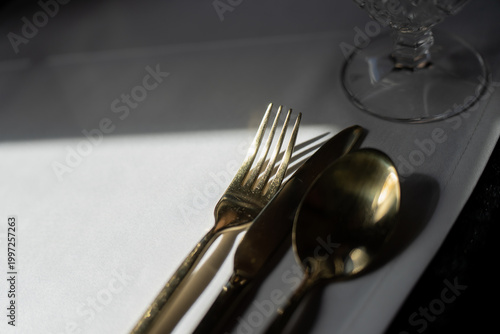High angle view of premium golden silverware and polished glassware on a white tablecloth, highlighting elegant hospitality standards for fine dining and banquet events