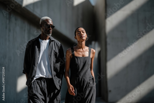A stylish couple walks through a well-lit urban setting, demonstrating a blend of contemporary fashion and modern architecture that speaks to sophistication and simplicity.
