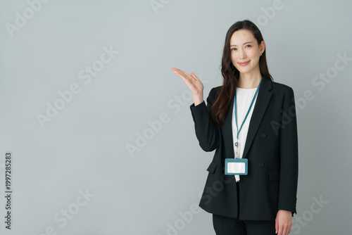 Konstfotografi グレーバックの手のひらを広げるポーズをする若いスーツの日本人女性