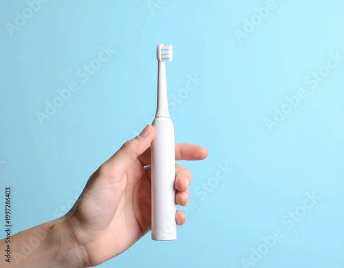 hand holding modern electric toothbrush on light blue background, dental care hygiene, oral health routine, bathroom accessory, sonic cleaner
