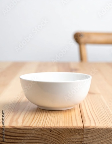 Empty white ceramic bowl sitting on rustic light wooden table, kitchenware for food photography, rustic home dining setting, clean kitchen interior