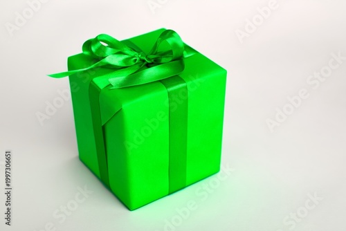 Bright Green Gift Box is Wrapped Neatly With a Satin Bow on a Light Gray Back...