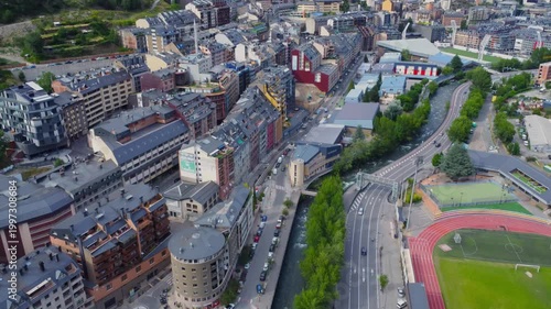 An expansive aerial shot showcasing the picturesque capital city of Andorra la Vella nestled within the stunning Pyrenees mountain range. The footage captures the urban landscape with its buildings, r