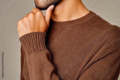 Thoughtful Man Poses in Brown Sweater With Hand on Chin in Studio Setting