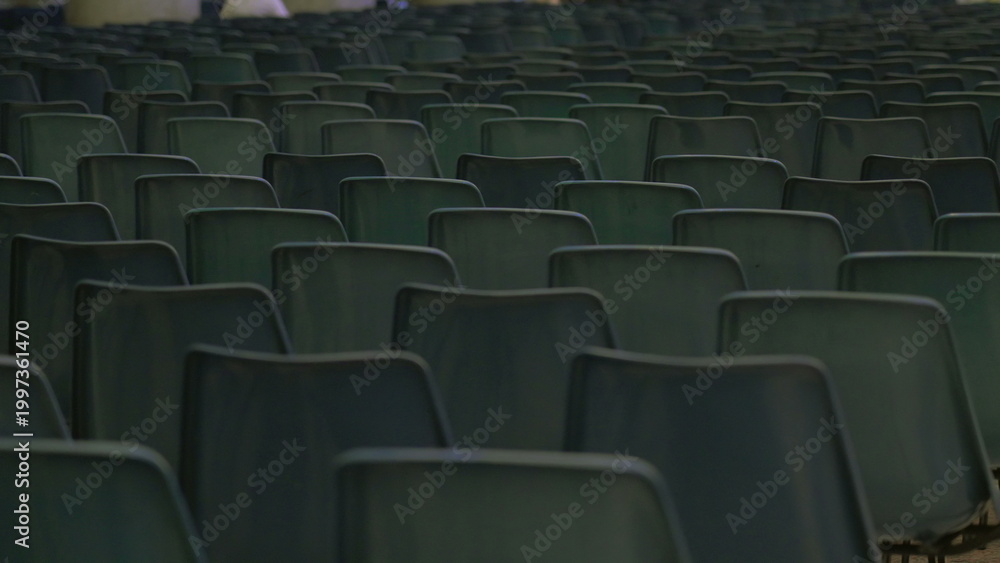 Fototapeta premium Dense rows of empty green plastic chairs closely arranged in symmetrical pattern inside large hall prepared for public gathering or conference