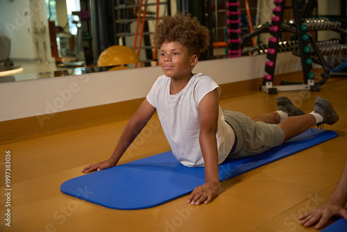 Happy boy practicing yoga indoors on blue exercise mat