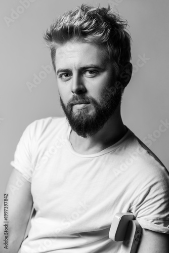 Black and white shot of calm attractive man with beard posing for portrait looking at camera with healthy skin isolated on gray background