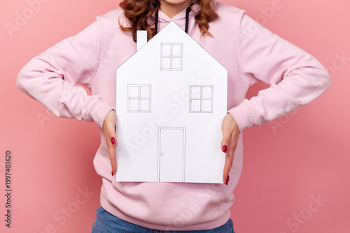 Cropped closeup view of faceless woman holding big paper house buying property for business or life isolated on pink background