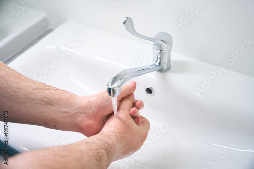 Adult man washing hands at bathroom sink during daytime