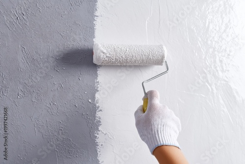 Person Painting a Wall With a Roller in a Light Grey Color During a Home Impr...