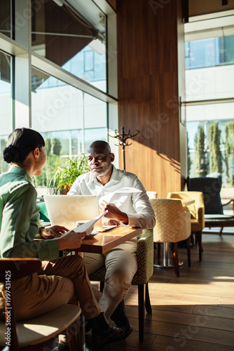Two business professionals meeting with laptop in sunlit cafe