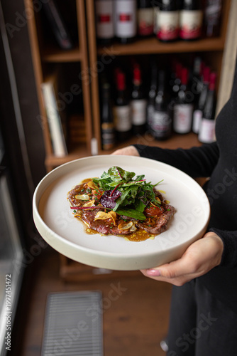 Quadro em tela Fresh beef carpaccio with greens and sauce served on plate held by waiter in res