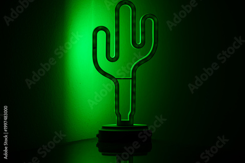 Green neon cactus lamp glowing in dark background.