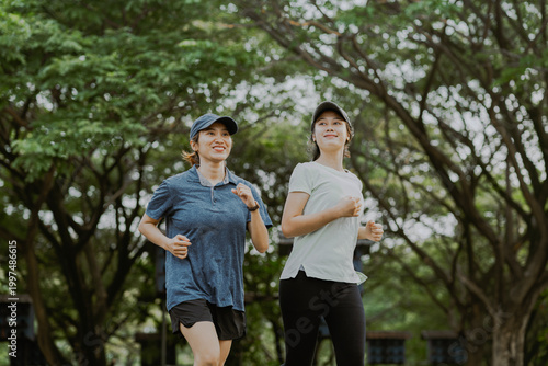 Two asian female friends or sisters doing sport activities on the park. Running, stretching, jogging in the morning. Healthy lifestyle concept.