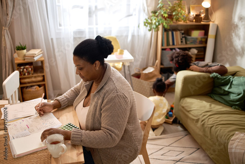 Photos African American mother managing household bills while children playing in background at home