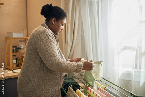 Fotografie Black woman drying laundry at home, managing household chores in low income living conditions