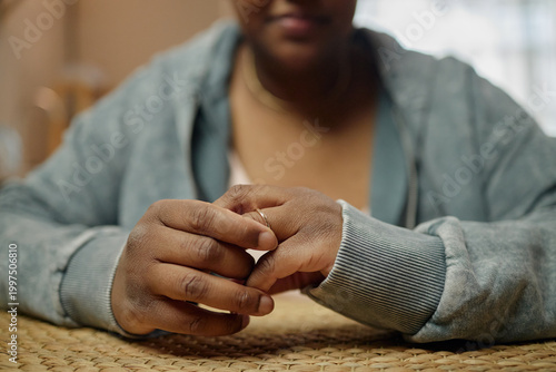 Photography Close up of Black woman removing wedding ring while clasping hands at table, conveying financial stress and family hardship