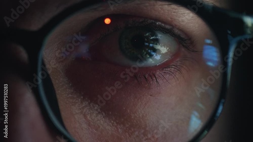 Information overload reflected in human eye behind glasses as glowing screen light flickers in pupil. Close up Eye scans endless data and news feeds showing information overload and digital stress.