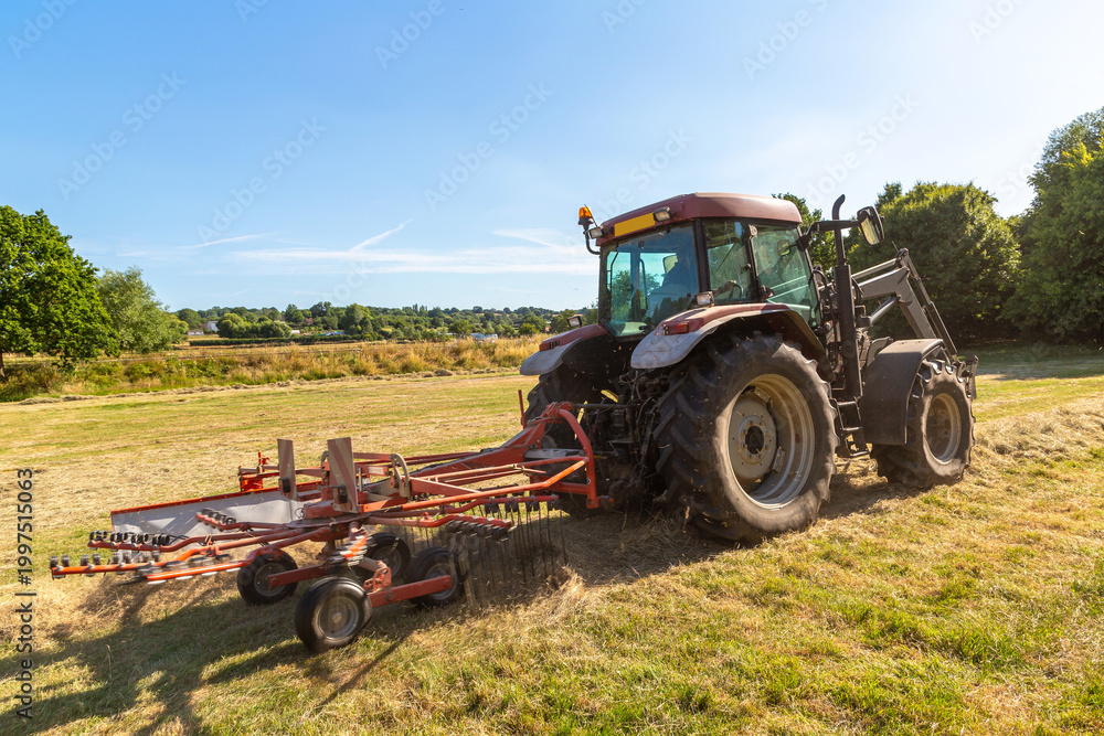 Fototapeta premium Agricultural Tractor Raking Hay on Field in East Sussex, England, UK near Bodiam Village