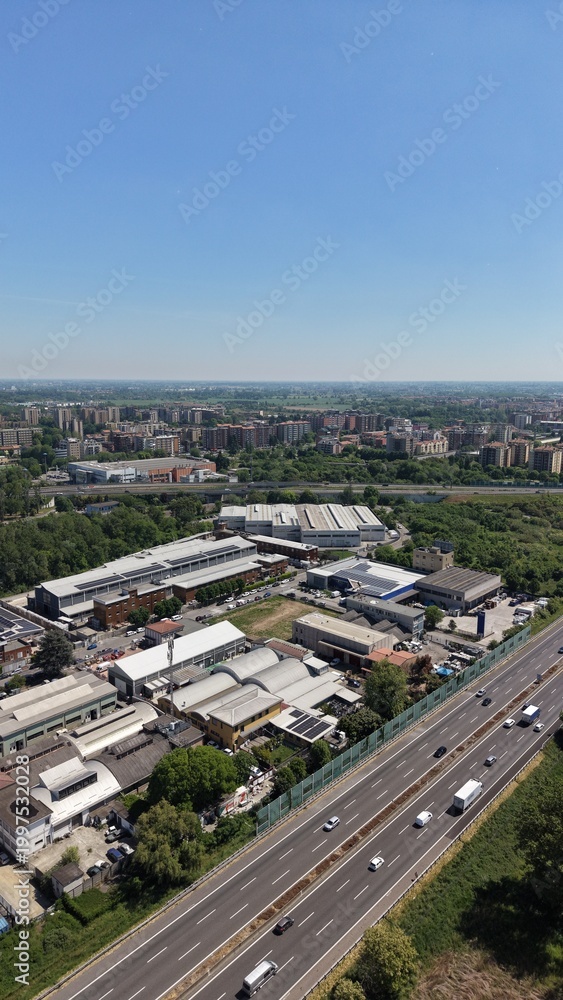 Obraz premium Aerial View of a bustling industrial landscape: A bird's-eye view unveils a vibrant scene of an industrial complex, crisscrossed by a busy highway, under a clear, endless blue sky.