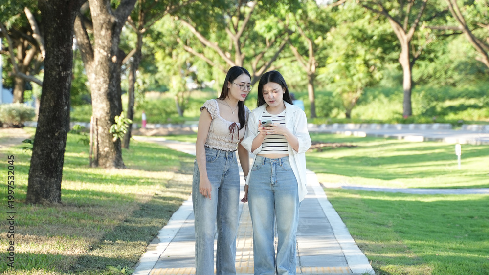 Naklejka premium Young Women Walking and Using Smartphone in Green Park