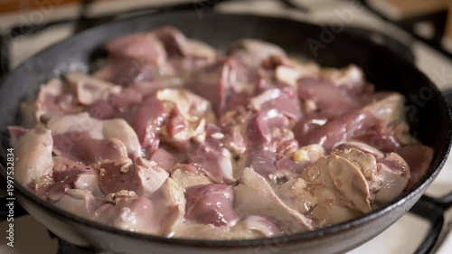 Fresh raw chicken livers are searing in a cast iron skillet on a hot stovetop, browning and sizzling as they cook. Concept of home cooking, traditional offal recipes, and nutrition.