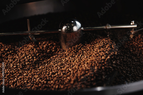 Foto Roasted coffee beans being mixed by metal agitator in roaster drum, Roasting sho