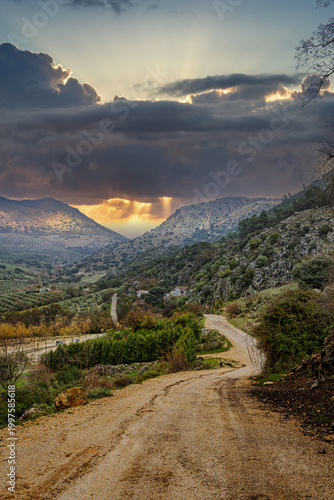 Camino rural sinuoso en la Sierra de Grazalema bajo un cielo dramático con rayos de sol crepusculares concepto de esperanza redención y misticismo en un paisaje de montaña místico al atardecer en Anda