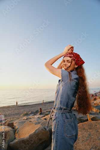 lifestyle woman in modern boho-western denim street style with red bandana smiling by the beach at sunset in warm film color tones