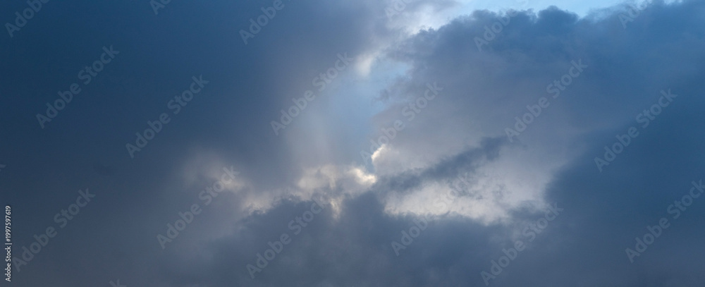 Fototapeta premium Sunbeams breaking through dark storm clouds on dramatic blue-grey sky