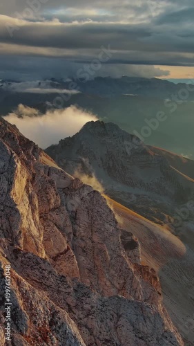 Aerial around view of amazing rocky mountains in clouds at sunset. Vertical video 4k