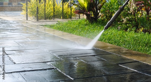 A high-pressure water jet cleans a dark stone patio effectively removing dirt and grime to reveal the clean surface underneath in a garden
