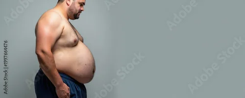 Panel kuchenny z motywem Overweight man looks down at large belly. Unhealthy guy shows excess fat accumulation around midsection. He stands shirtless wearing blue shorts with copy space.